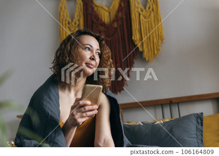 Middle aged woman uses mobile phone while sitting in bed in morning 106164809