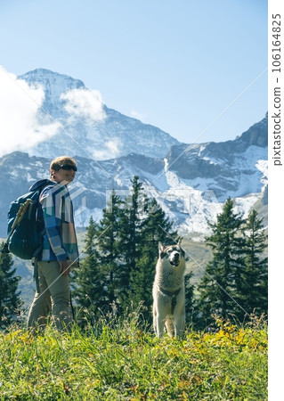 Sporty woman with husky dog standing in front of snow mountains and enjoying view of Switzerland nature. Wanderlust, sport, beauty in nature, traveling with a pet Sporty woman with husky dog standing in front of snow mountains and enjoying view of Switzerland nature. Wanderlust, sport, beauty in nature, traveling with a pet 106164825