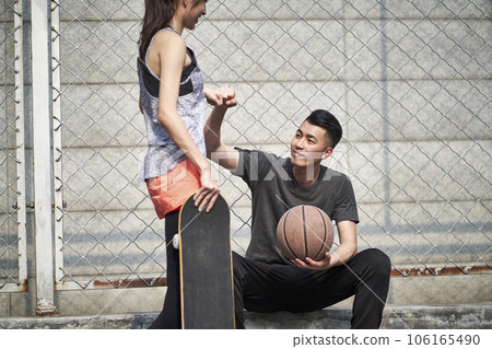 young asian adult male basketball player and female skateboarder bumping fists on a outdoor court young asian adult male basketball player and female skateboarder bumping fists on a outdoor court 106165490