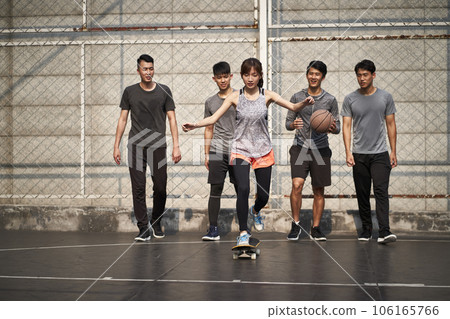 young asian woman skateboarder skateboarding outdoors with friends watching from behind 106165766