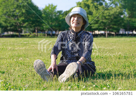 一位老一代婦女坐在草坪上，戴著微笑的帽子 106165781
