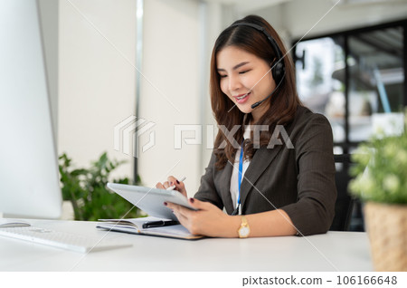 A professional Asian female call centre operator with a wireless headset using her digital tablet 106166648