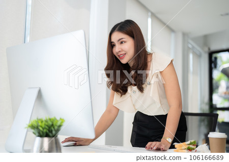 A professional Asian businesswoman is bending over a table and looking at her computer screen 106166689