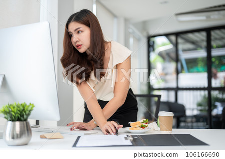 A focused Asian businesswoman is bending over a table and looking at her computer screen 106166690
