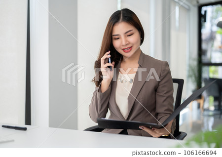 A gorgeous Asian businesswoman is reading some details on a document while talking on the phone 106166694