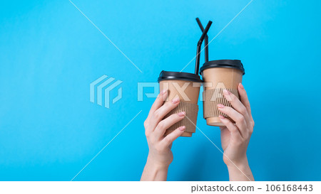 A woman holds two cardboard cups with coffee on a blue background. 106168443