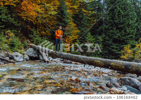 Hiker man staying on a log over the mountain river in autumnal forest. Hiker man staying on a log over the mountain river in autumnal forest. 106168482