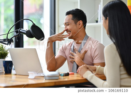 Cheerful gay male radio host discussing various topics with guest while streaming live audio podcast from studio Cheerful gay male radio host discussing various topics with guest while streaming live audio podcast from studio 106169110