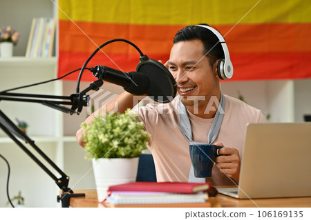 Smiling gay man radio host in headphone talking through microphone for recording conversation for channel 106169135