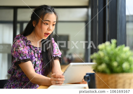 Surprised young woman looking at digital tablet reading good news online, delighted by new opportunity 106169167