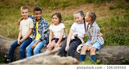 Cheerful playful kids sitting on log in forest on sunny day. Going hiking, walking, having active weekends 106169568