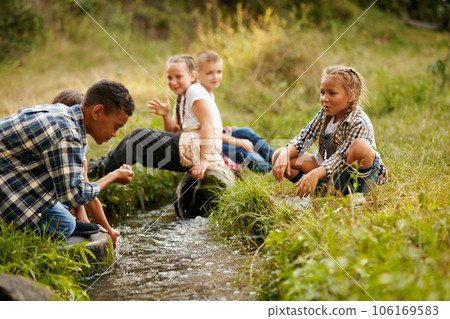 Children playing near little river in forest, drinking water. Warm sunny day activity. Refreshment 106169583