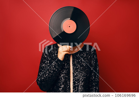Woman in sequin dress holding vinyl record head isolated over red background Woman in sequin dress holding vinyl record head isolated over red background 106169696
