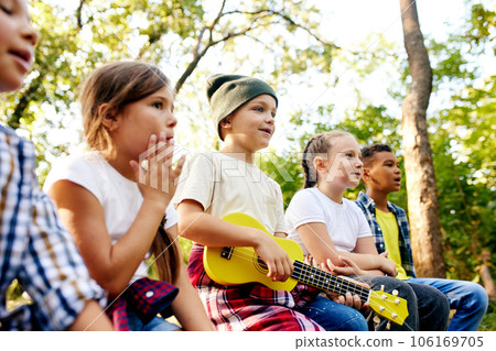 Happy kids sitting on log in forest on sunny day, playing guitar, having fun. Going hiking, walking, active weekends 106169705