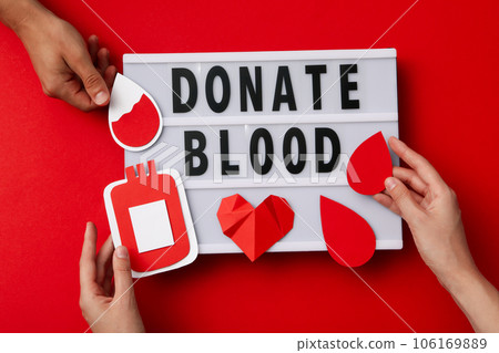 Paper container of blood in hand with red heart on red background. Blood donation Paper container of blood in hand with red heart on red background. Blood donation 106169889