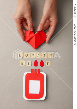 Paper blood container in hand with red heart on gray background. Blood donation 106169937