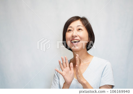 Middle-aged woman looking up and clapping with a smile Middle-aged woman looking up and clapping with a smile 106169940