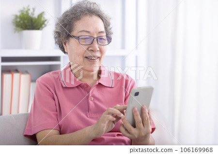 Senior woman sitting couch browsing mobile phone 106169968