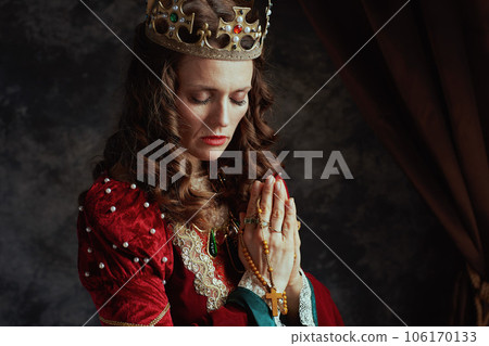 medieval queen in red dress with rosary and crown praying 106170133