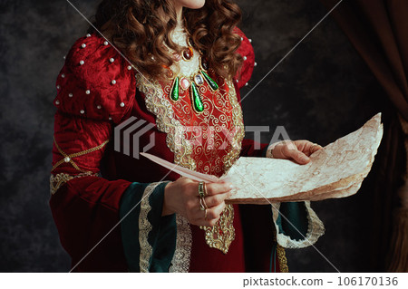Closeup on medieval queen in red dress with parchment 106170136