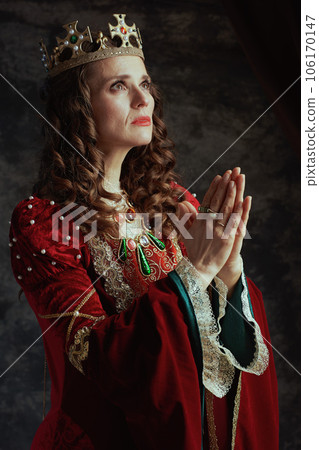 medieval queen in red dress with crown praying 106170147