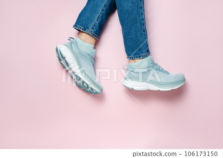 Women legs in blue jeans and new green blue modern running shoes on pink background. Stylish monochrome shoes for active people that incorporate new health technology. Top view 106173150