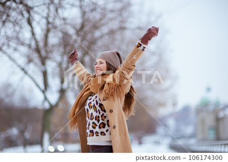 smiling modern woman in brown hat and scarf in camel coat 106174300