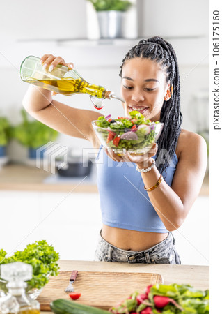 A young African American woman prepares a healthy leafy salad, tossing it with olive oil A young African American woman prepares a healthy leafy salad, tossing it with olive oil 106175160