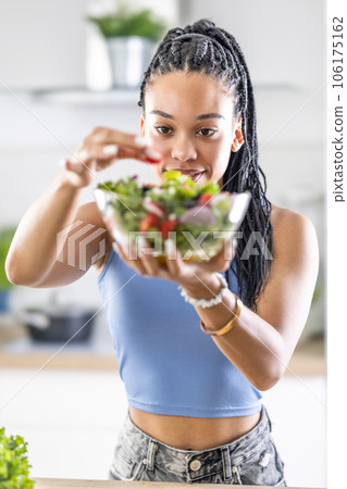Young African American woman prepares healthy salad, adds tomatoes Young African American woman prepares healthy salad, adds tomatoes 106175162