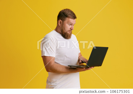 Bearded man emotional looking on laptop, working, shopping online against yellow studio background Bearded man emotional looking on laptop, working, shopping online against yellow studio background 106175301