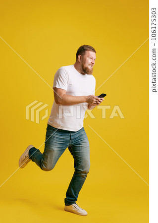 Texting on way. Man in casual clothes texting on mobile phone against yellow studio background 106175303
