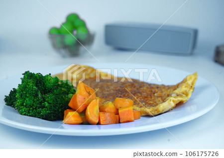 A healthy breakfast with scrambled eggs, boiled broccoli, and sliced boiled carrots, served on a white plate. 106175726