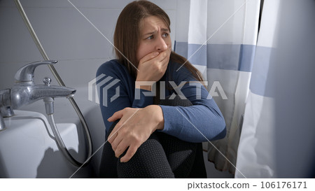 Young woman feeling scared hiding in bathroom and closing her mouth to stop screaming. Concept of domestic violence victim, stress, danger at home, fear and disaster. 106176171
