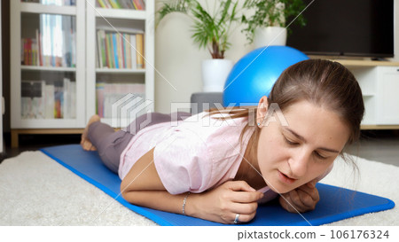 Young woman falling on fitness mat after doing plank during fitness training. Concept of healthcare, sports and yoga at home. Young woman falling on fitness mat after doing plank during fitness training. Concept of healthcare, sports and yoga at home. 106176324