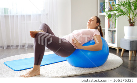 Young woman struggling doing hard fitness exercise on fitball during home training. Concept of healthcare, sports and yoga at home. 106176325