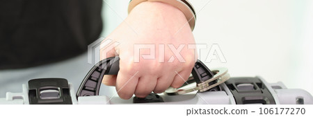 Human hand is connected to suitcase with handcuffs close-up. 106177270