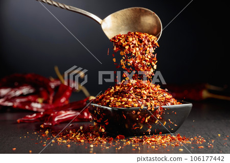 Chilli flakes are poured into a black dish. Chilli flakes are poured into a black dish. 106177442