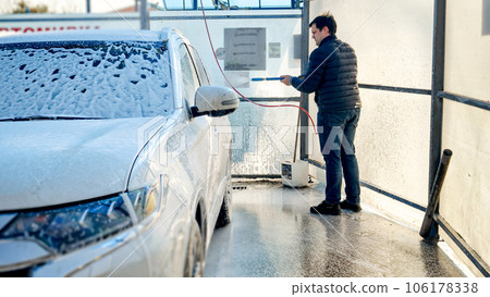 Young man washing his dirty car at self service carwash. Automobile care, transport cleaning, dirty car. 106178338