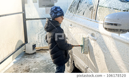 Smiling boy helping washing car with brush and foam. Concept of parenting, children helping parents and automobile care. 106178520