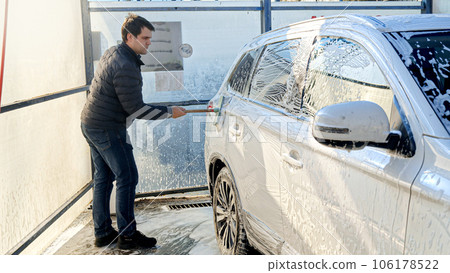 Young man washing his car at self-service carwash. Automobile care, transport cleaning, dirty car. 106178522