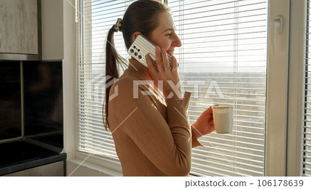 Young woman having coffee break in office and talking by phone. People in morning, beautiful cityscape, having break at office. Young woman having coffee break in office and talking by phone. People in morning, beautiful cityscape, having break at office. 106178639