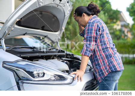 Asian woman check for repair under the hood of broken down car on the side of the road. 106178806