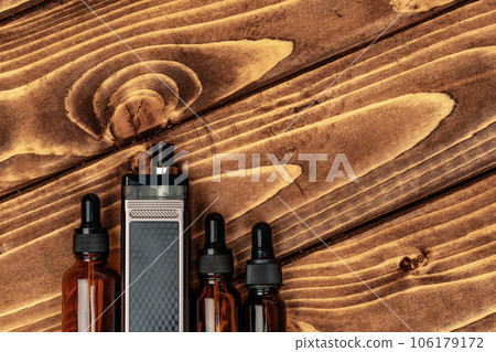 Vape and vape juice bottles on brown wooden background 106179172