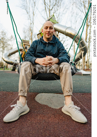 Smiling bald man sitting on a swing in a playground 106179201