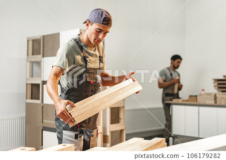 Young carpenter man looking and choosing wood plank at workshop in carpenter wood factory 106179282