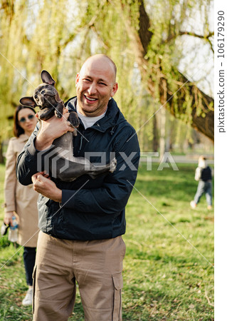 Man holding his french bulldog puppy in hands while having a walk in the park 106179290