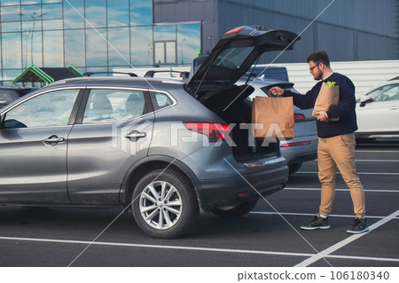happy man put groceries bag in car trunk 106180340