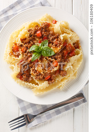 Italian Reginette pasta with bolognese sauce closeup on the plate on the wooden table. Vertical top view 106180409