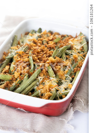 A traditional green bean casserole topped with French Fried Onions and cream of mushroom on white marble. Close up A traditional green bean casserole topped with French Fried Onions and cream of mushroom on white marble. Close up 106181264