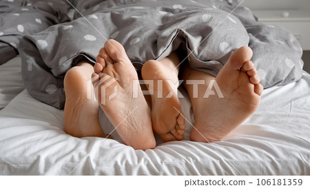 Couple's feet, exploring each other's intimacy under a cozy blanket on a soft bed. Ideal for portraying the concept of family love and the significance of intimacy in a relationship. 106181359